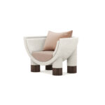 Modern armchair with a curved frame, upholstered in soft fabric, featuring ribbed walnut legs, and plush beige cushions, by Nolita Harbour. Anna Armchair 45 degree view