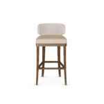 Elegant bar chair with a curved upholstered backrest, beige cushioned seat, and walnut wood legs with metal accents, designed by Nolita Harbour for modern bar settings. Front View