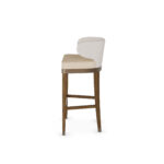 Elegant bar chair with a curved upholstered backrest, beige cushioned seat, and walnut wood legs with metal accents, designed by Nolita Harbour for modern bar settings. Side View