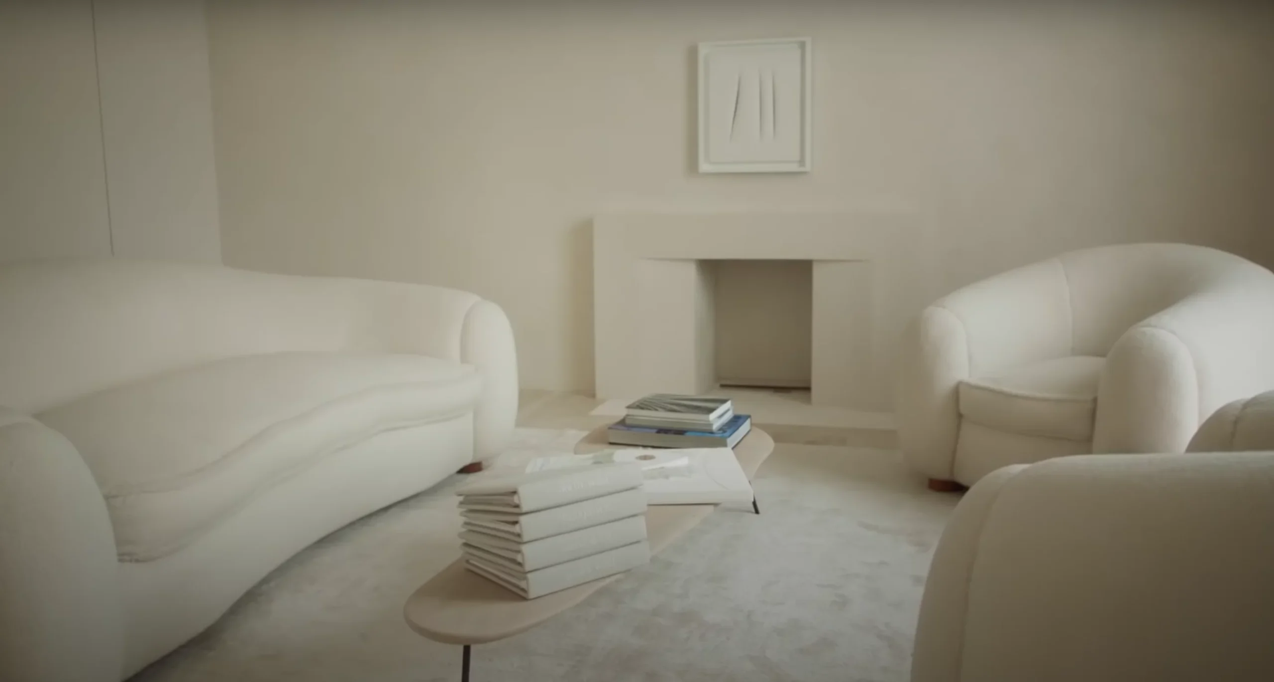 A monochromatic, modern living room featuring white curved sofas, a sleek coffee table with stacked books, and a neutral fireplace, creating a serene and minimal aesthetic. - Nolita Harbour