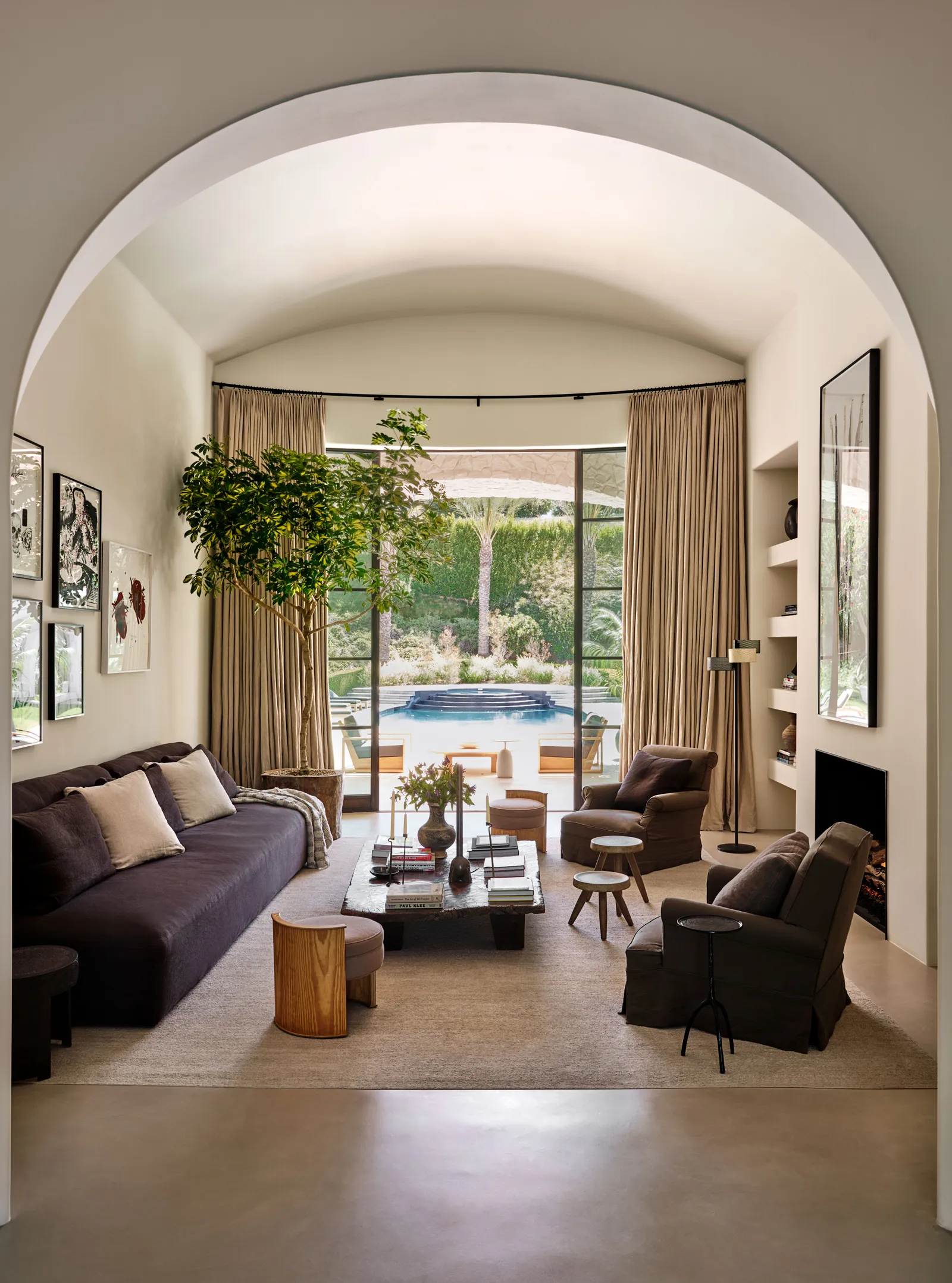 A cozy yet elegant living space with a vaulted ceiling, soft earthy tones, and a seamless indoor-outdoor transition. Large glass doors open to a lush backyard with a swimming pool, enhancing the tranquil ambiance. - Nolita Harbour