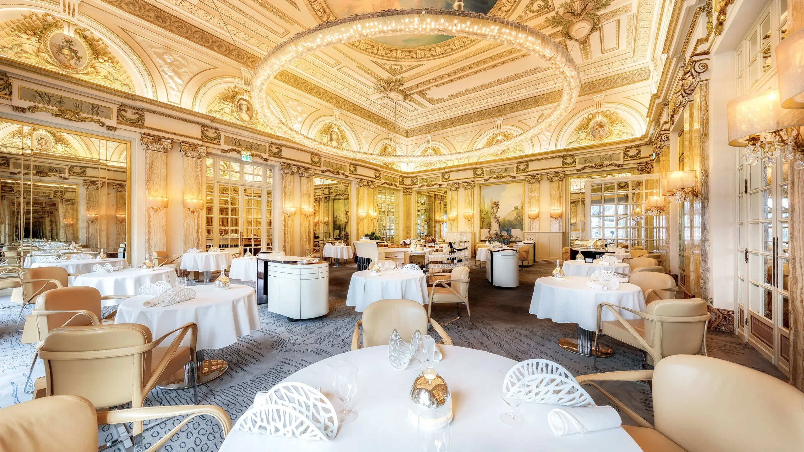 "Exquisite dining room of Le Louis XV – Alain Ducasse at the Hôtel de Paris in Monaco, showcasing lavish 18th-century-inspired décor with gilded moldings, crystal chandeliers, and marble floors. The elegantly set tables, surrounded by plush seating, create an atmosphere of refined luxury, being one of the most expensive restaurant, reflecting the restaurant's three Michelin-starred culinary excellence." - Nolita Harbour 