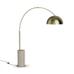 Nils Floor Lamp, a sculptural floor lamp by Nolita Harbour in travertine and brass, with arched frame and a dome shade.