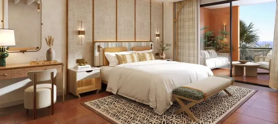 Elegant Mediterranean-style hotel room with king-size bed, warm neutral décor, ceiling fan, private balcony with seating, and sea views.