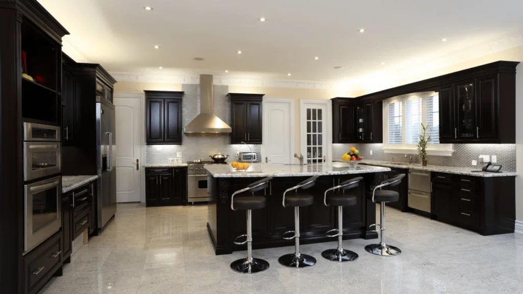 Modern kitchen island with a marble countertop, dark tiled base, wooden counter stools with black seats, brass faucet, and geometric backsplash.