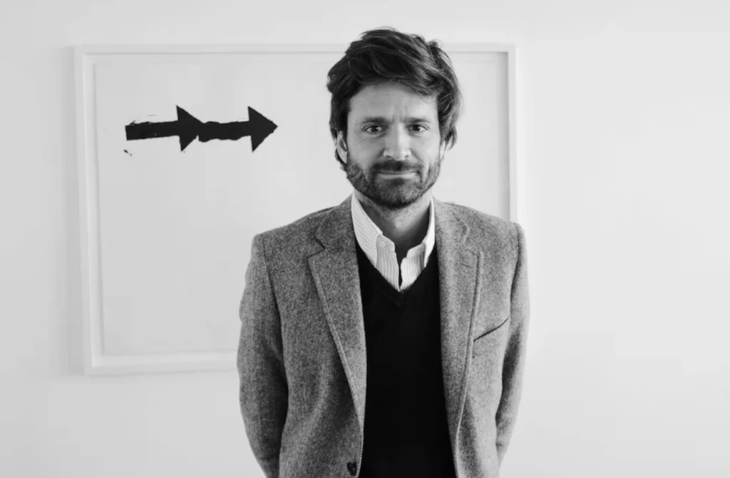 Black-and-white portrait of a contemporary minimalist architect Joseph Dirand, expressing quiet confidence and intellectual restraint against a gallery-like backdrop.
