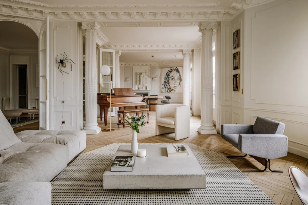 Elegant Parisian apartment interior with classical columns, ornate ceiling moldings, herringbone parquet flooring, and contemporary furniture, illustrating refined urban living through a harmonious blend of heritage architecture and modern interior design.
