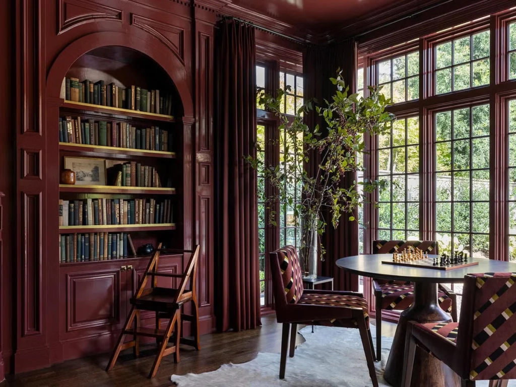 Luxury reading corners in modern homes featuring custom built-in bookshelves, sculptural armchairs, layered textiles, and natural light—from a rich burgundy-paneled library with arched shelving to a contemporary glass-walled study, a minimalist Scandinavian nook, a deep blue velvet window seat library, and a Parisian-inspired corner with ornate moldings and vibrant textiles.