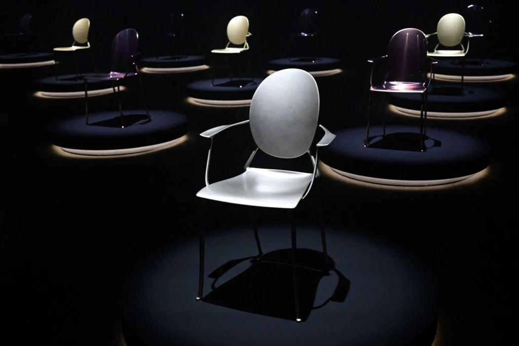 Sculptural contemporary chairs displayed on illuminated circular platforms, showcasing innovative forms and finishes at Salone del Mobile 2026.