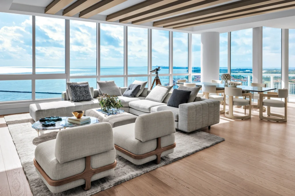 Expansive open-plan luxury living room in a Miami waterfront penthouse with floor-to-ceiling glass walls, contemporary designer furnishings, and panoramic ocean views flooding the interior with natural light.