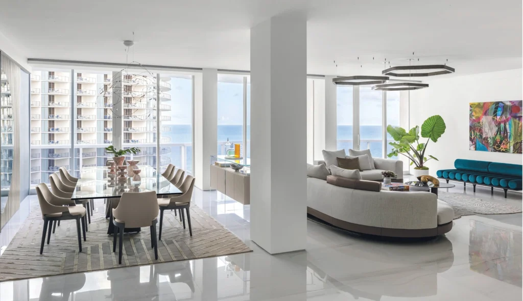 Expansive open-plan luxury living room in a Miami waterfront penthouse with floor-to-ceiling glass walls, contemporary designer furnishings, and panoramic ocean views flooding the interior with natural light.