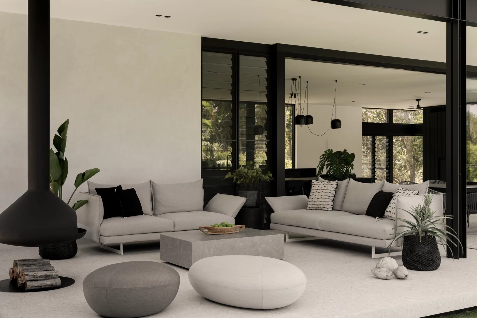 Modern living room with sleek gray sofas adorned with monochrome cushions, a central coffee table, a suspended black fireplace, and potted plants.