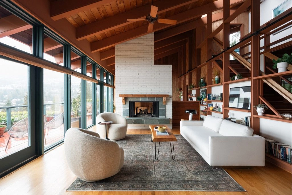 Spacious living room in a Vancouver luxury home with wooden beams, large windows, white brick fireplace, modern white sofa, cozy armchairs, and a patterned rug. Airy, elegant vibe.