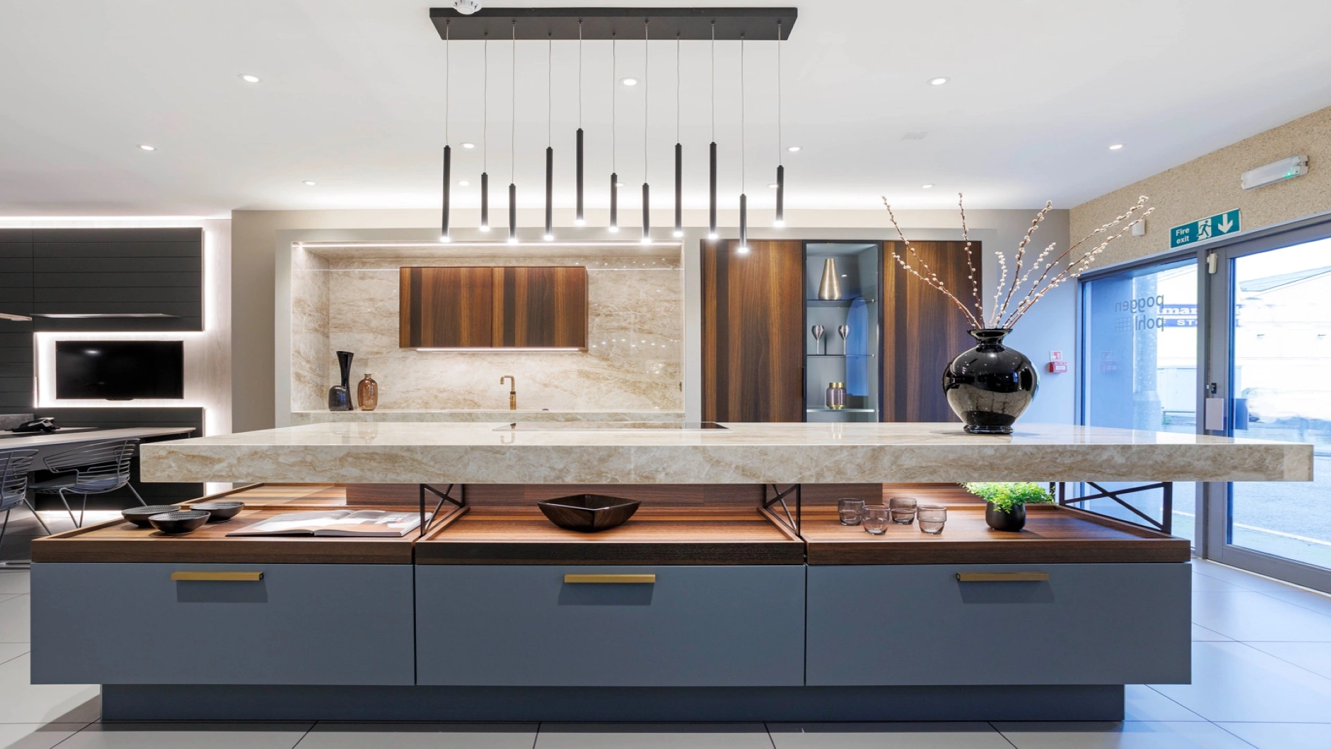 Modern luxury open kitchen with sleek design; features a large island with marble countertop, hanging black lights, and blue cabinets.