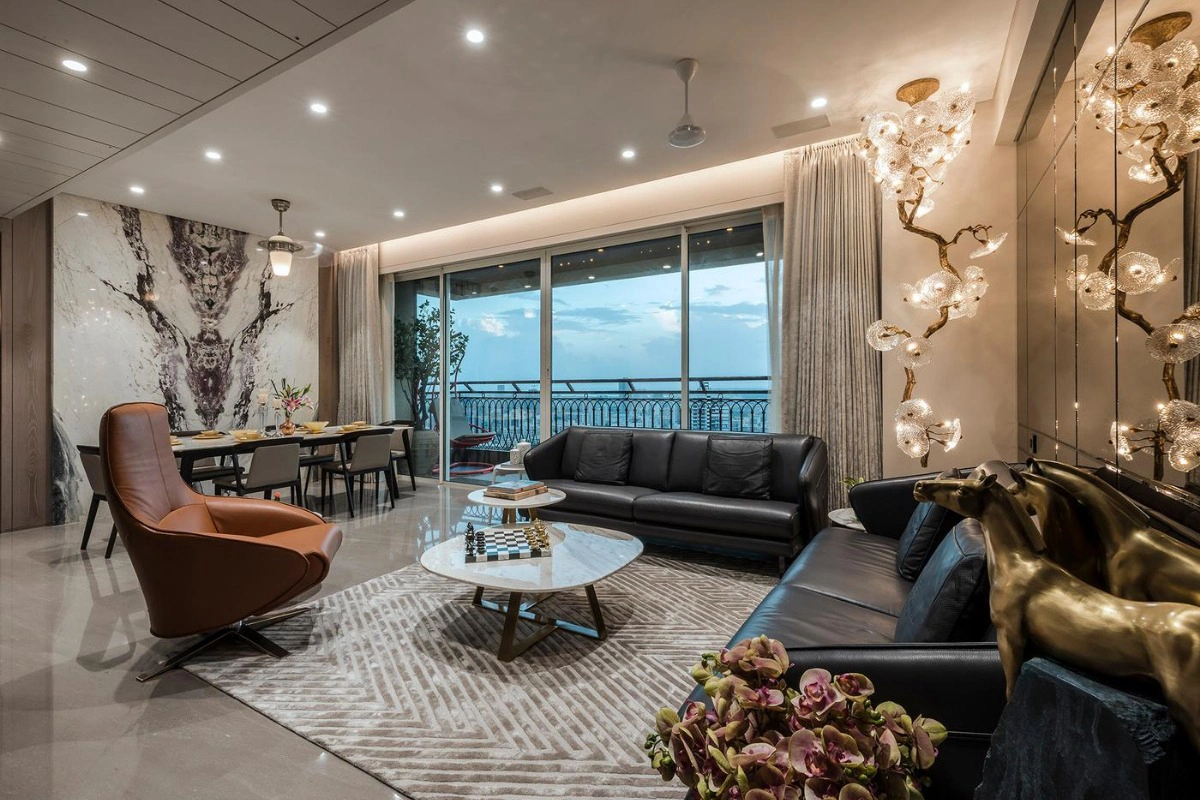 Modern living room with large windows showing an ocean view. Features include a black leather sofa, abstract wall art, golden horse sculptures, and ornate lighting, a demonstration of how luxury residential interiors are heavily influenced by hospitality design.