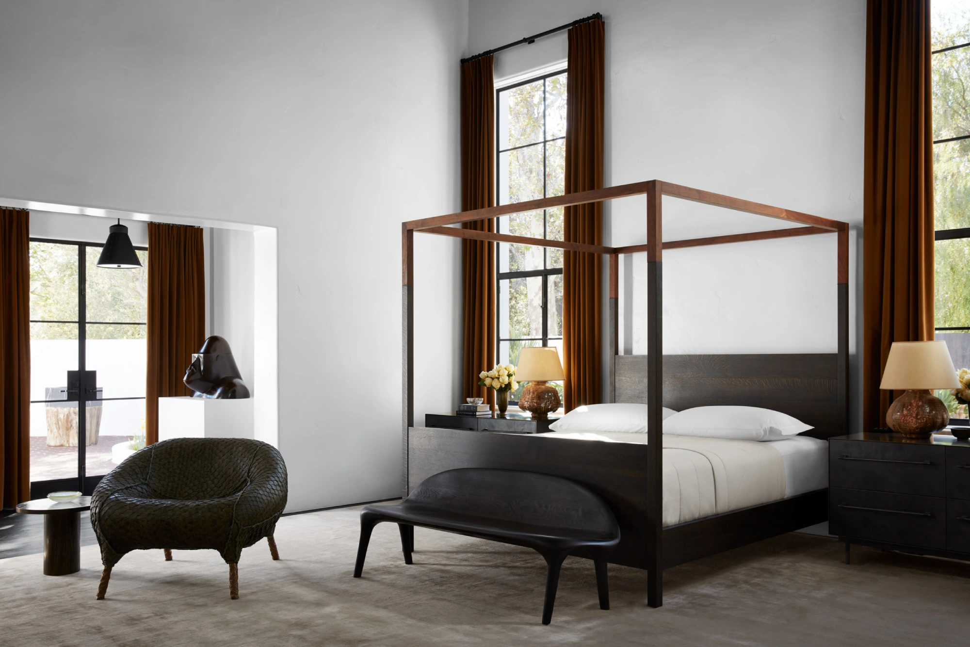 Modern bedroom with a dark wooden four-poster bed, white linens, and sleek black furniture. Tall windows with brown curtains add elegance and warmth.