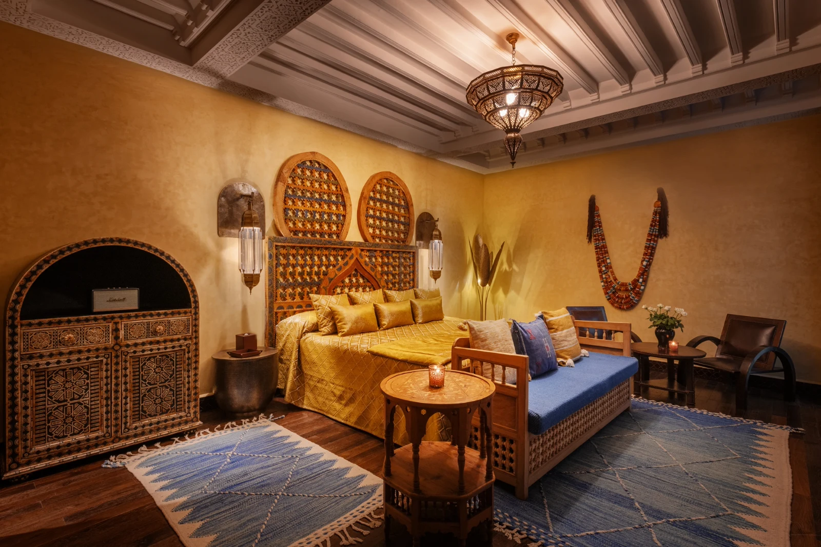 Warm Moroccan-style bedroom with golden walls, ornate patterns, a plush bed, blue rug, and ambient lighting, creating a cozy, inviting atmosphere.