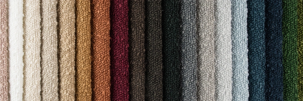 Close-up of vertically arranged textured bouclé fabric swatches in various colors, from pastel shades to dark tones, creating a visually rich and tactile display.