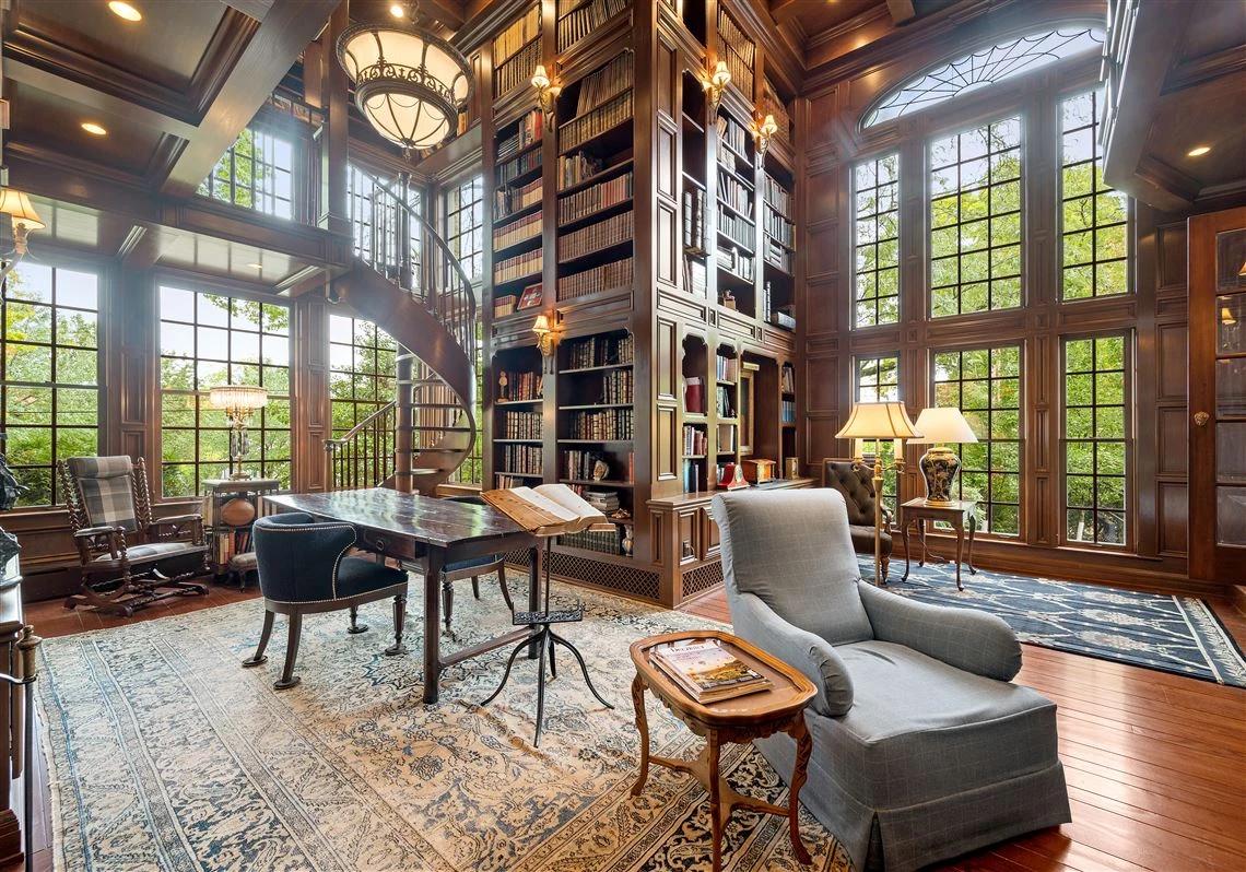 Luxurious library with tall bookshelves, spiral staircase, and large windows letting in natural light. Elegant furniture and warm, cozy ambiance, following the style of interior design for luxury homes.