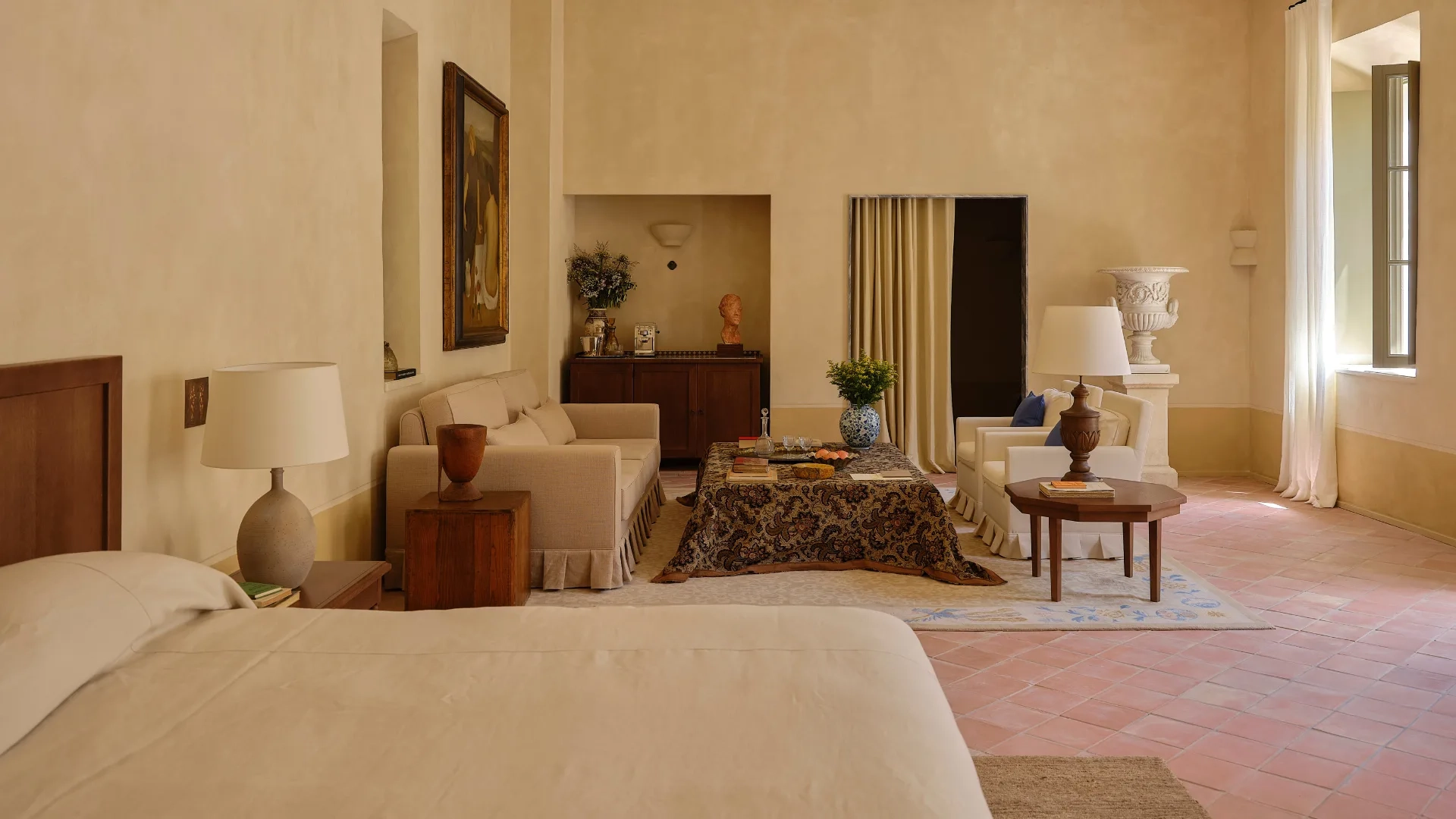 Luxury interior design bedroom with a large bed, elegant seating area, and soft beige tones. Natural light filters through a window, creating a serene ambiance.