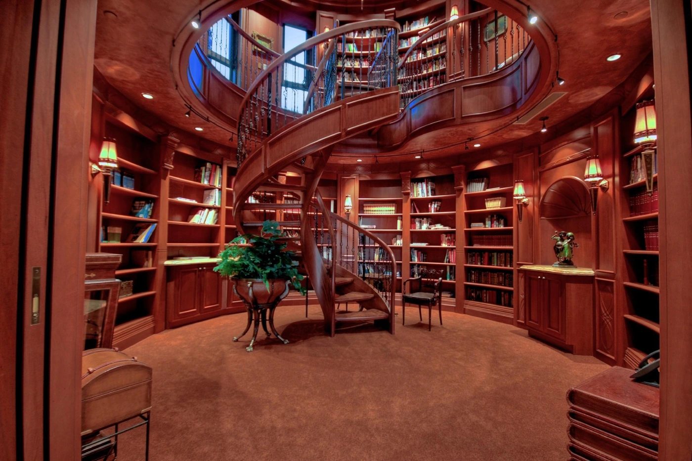 Luxurious circular library with rich wood tones. A spiral staircase leads to a second level of bookshelves. Warm lighting and elegant decor create a cozy, sophisticated atmosphere.