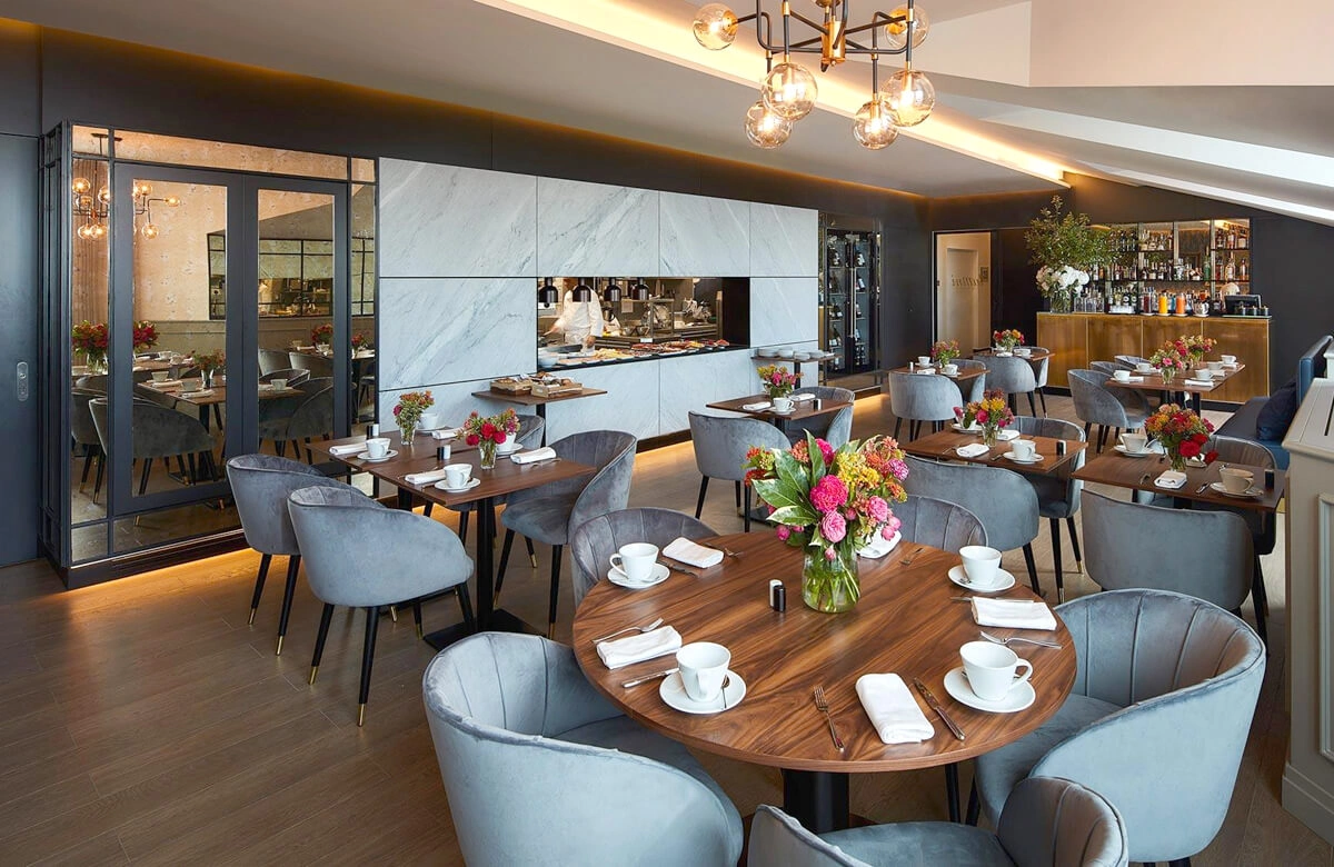 Stylish restaurant interior at Lumiares Hotel in Lisbon with round wooden tables, gray upholstered chairs, floral centerpieces, and place settings.