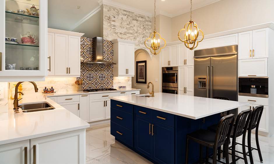 A modern kitchen with white cabinets, a blue island, gold fixtures, and three pendant lights. Stainless steel appliances add a sleek touch.