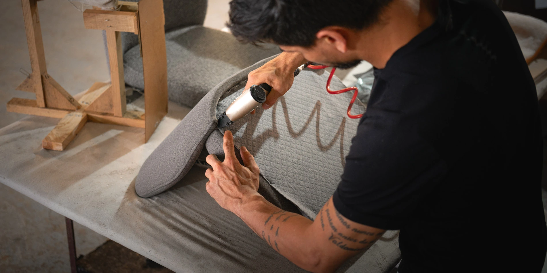 Artisan upholstering a chair with grey fabric using a power tool, highlighting the handmade upholstery process and craftsmanship in luxury furniture by Nolita Harbour.