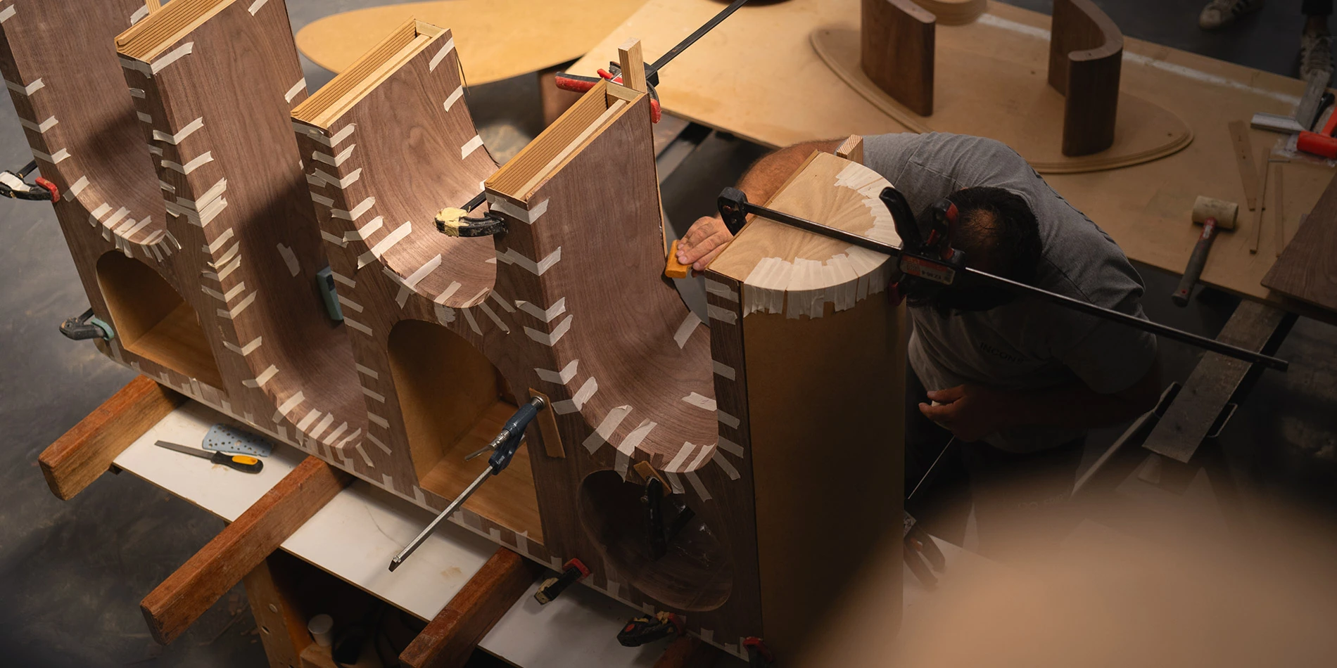 Craftsman assembling bespoke console with clamps and tape, highlighting material and structural quality in luxury furniture by Nolita Harbour.