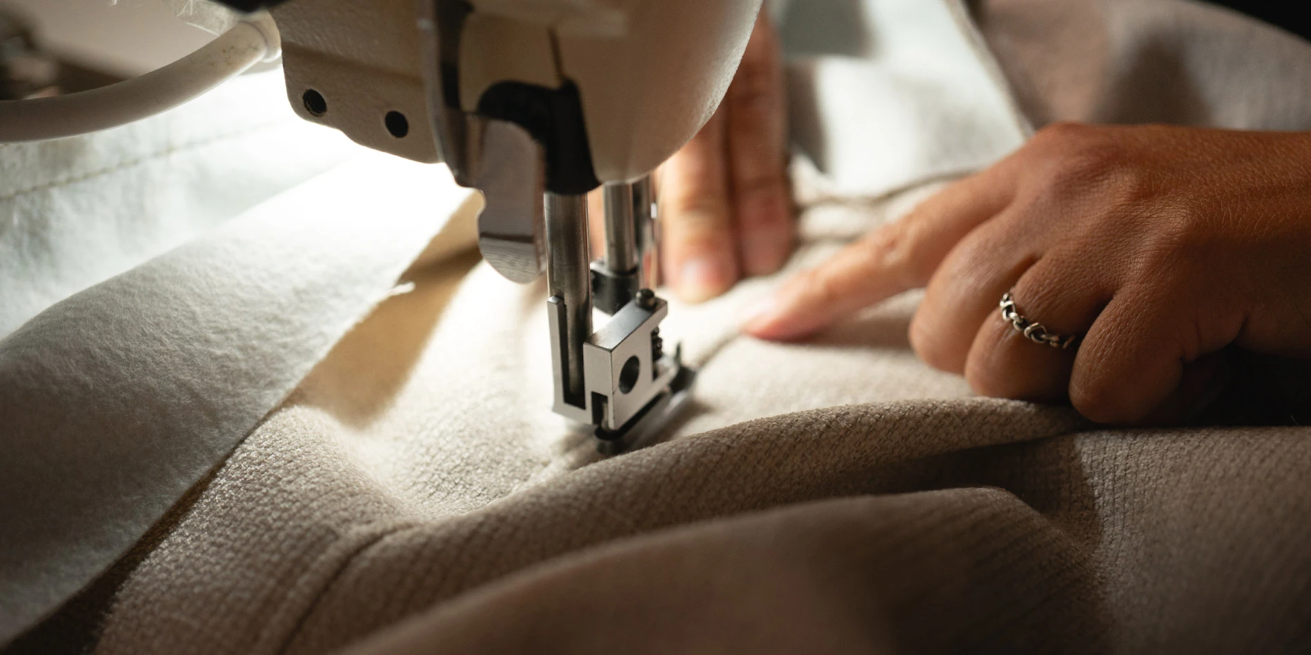 Artisan guiding premium fabric through an industrial sewing machine, showcasing precision stitching in the bespoke upholstery process for contemporary furniture by Nolita Harbour.