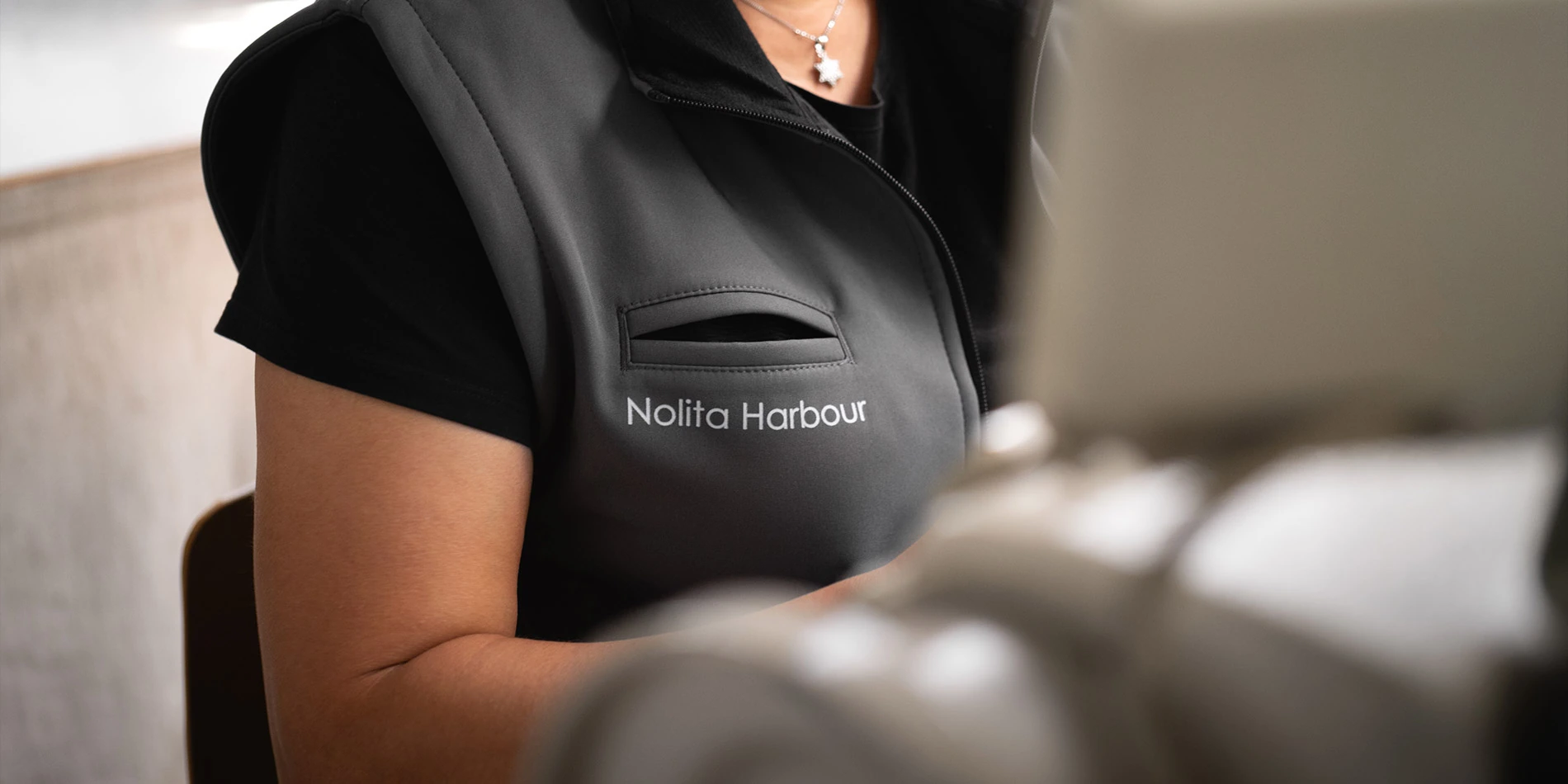 Artigiano con gilet brandizzato Nolita Harbour che supervisiona la fase di tappezzeria, evidenziando precisione e qualità nel processo di mobili artigianali su misura.