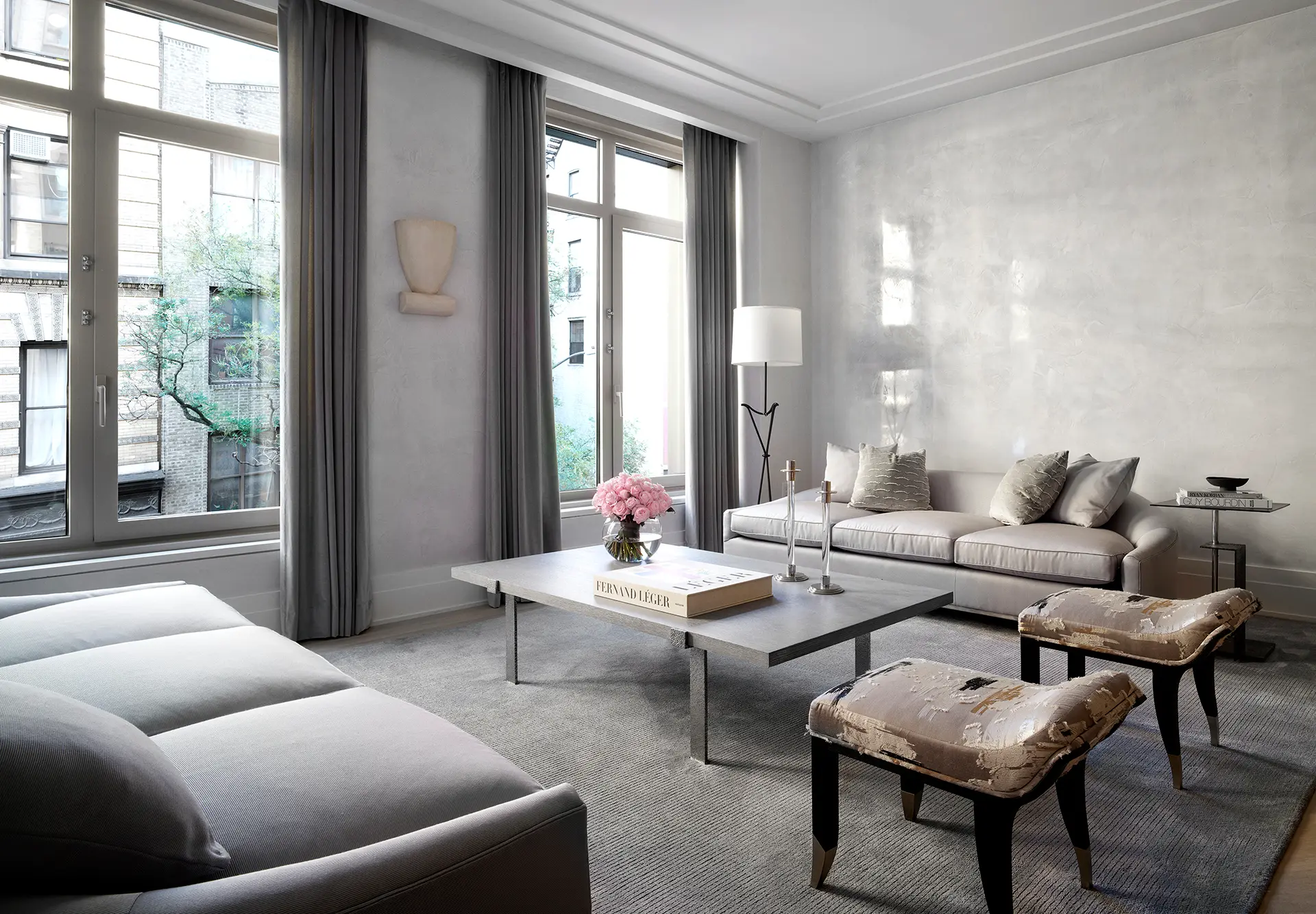 Living room at Bleecker Residences by Ryan Korban with modern decor, featuring neutral tones, large windows with gray curtains, a gray sofa, and elegant furnishings, creating a serene ambiance.