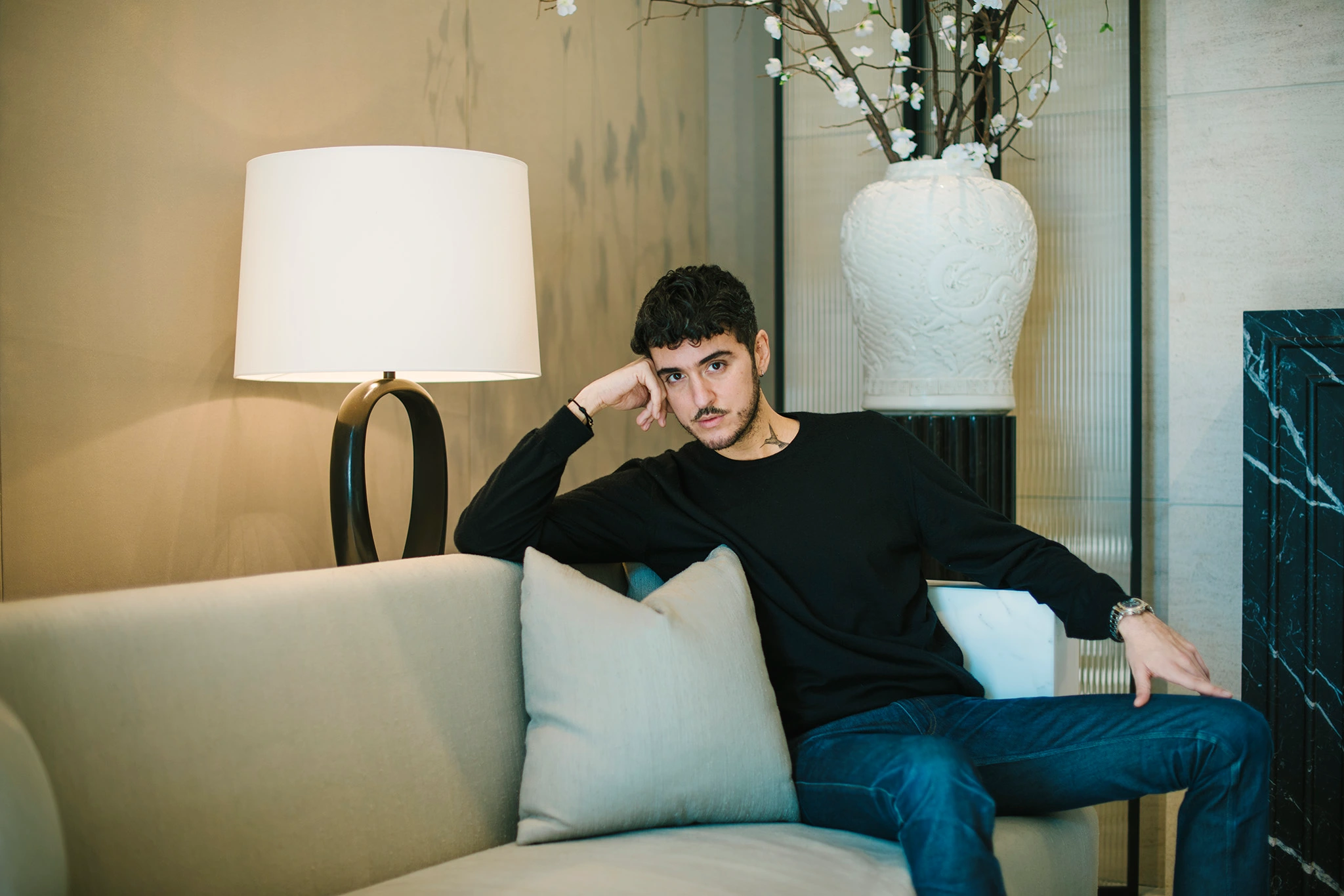 Interior designer Ryan Korban lounges on a beige sofa, resting his head on his hand.