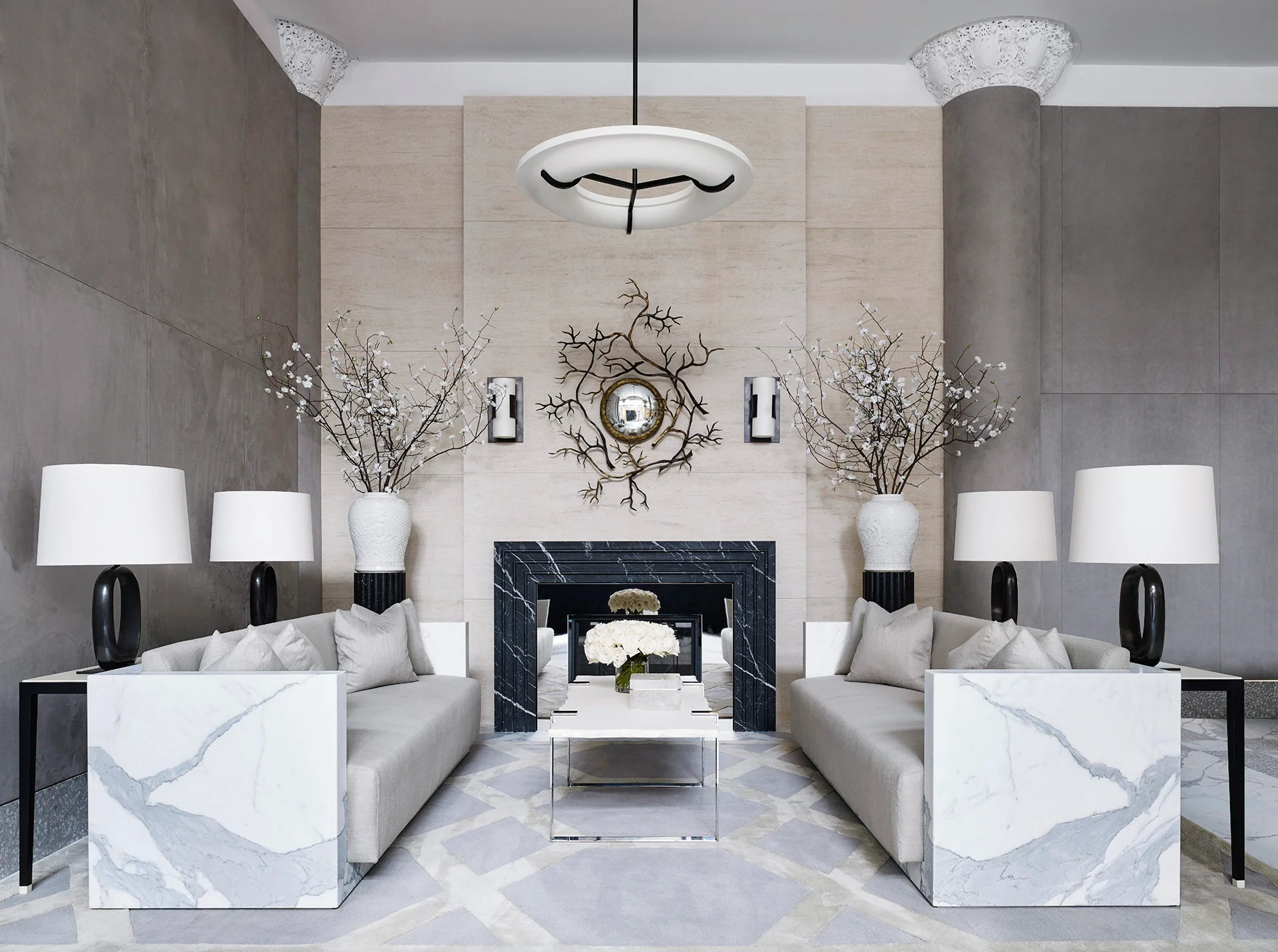 Luxurious living room by interior designer Ryan Korban with marble accents, symmetrical sofas, a black fireplace, and a large decorative mirror. Minimalist and elegant design.