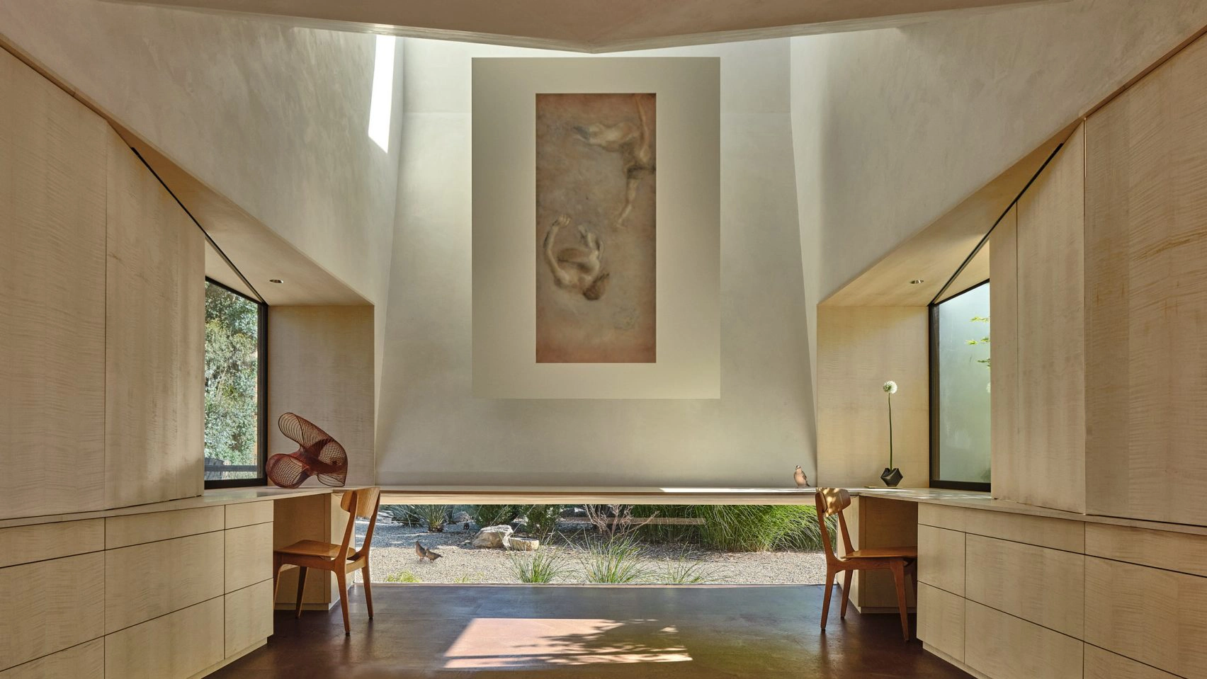 Spacious minimalist room with wooden cabinets, two chairs, large wall art, and a big window revealing a serene garden. The atmosphere is calm and natural.