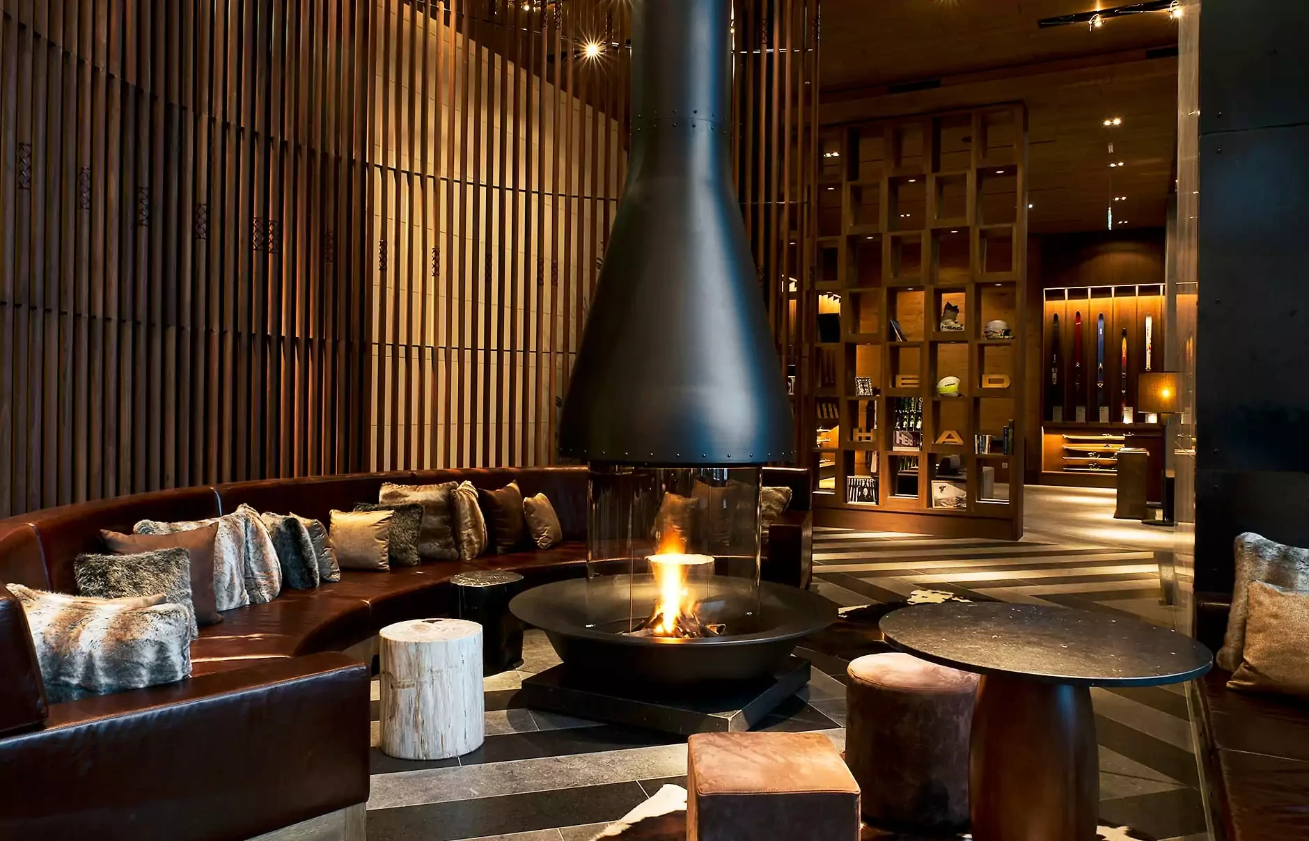 Modern lounge area at The Chedi Andermatt with a central hanging fireplace, leather seating, wooden accents, and warm ambient lighting—an inviting retreat among Swiss Alps resorts.