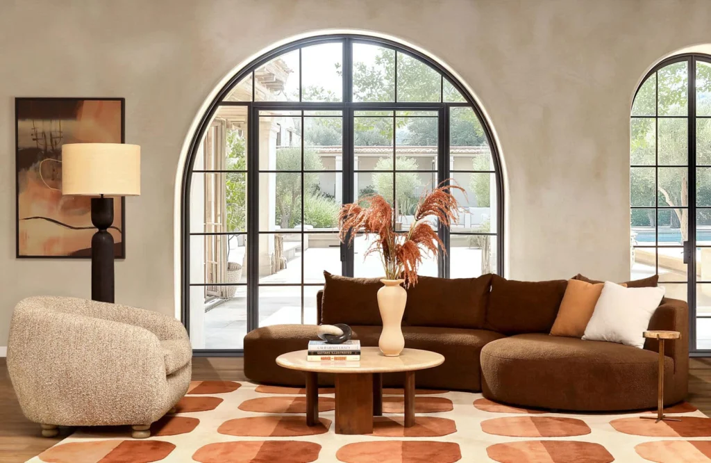 Inviting living room with large arched windows, brown sectional sofa, round chair, modern art, patterned rug, and elegant decor creating a warm, cozy atmosphere,