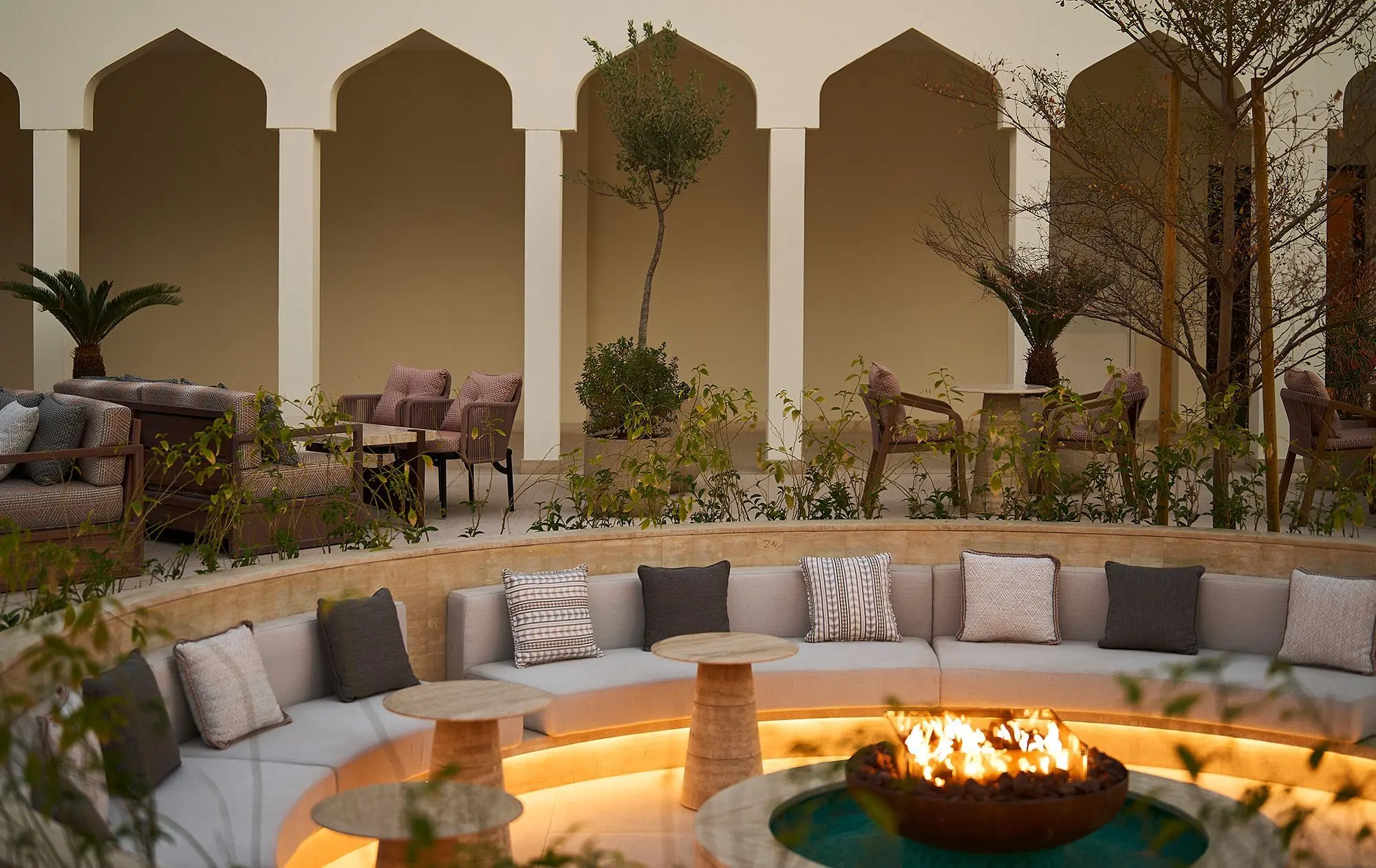 A cozy outdoor seating area at the Gerbou restaurant, decorated by Kristina Zanic,with a round fire pit at its center. Plush cushions line the circular bench. 
