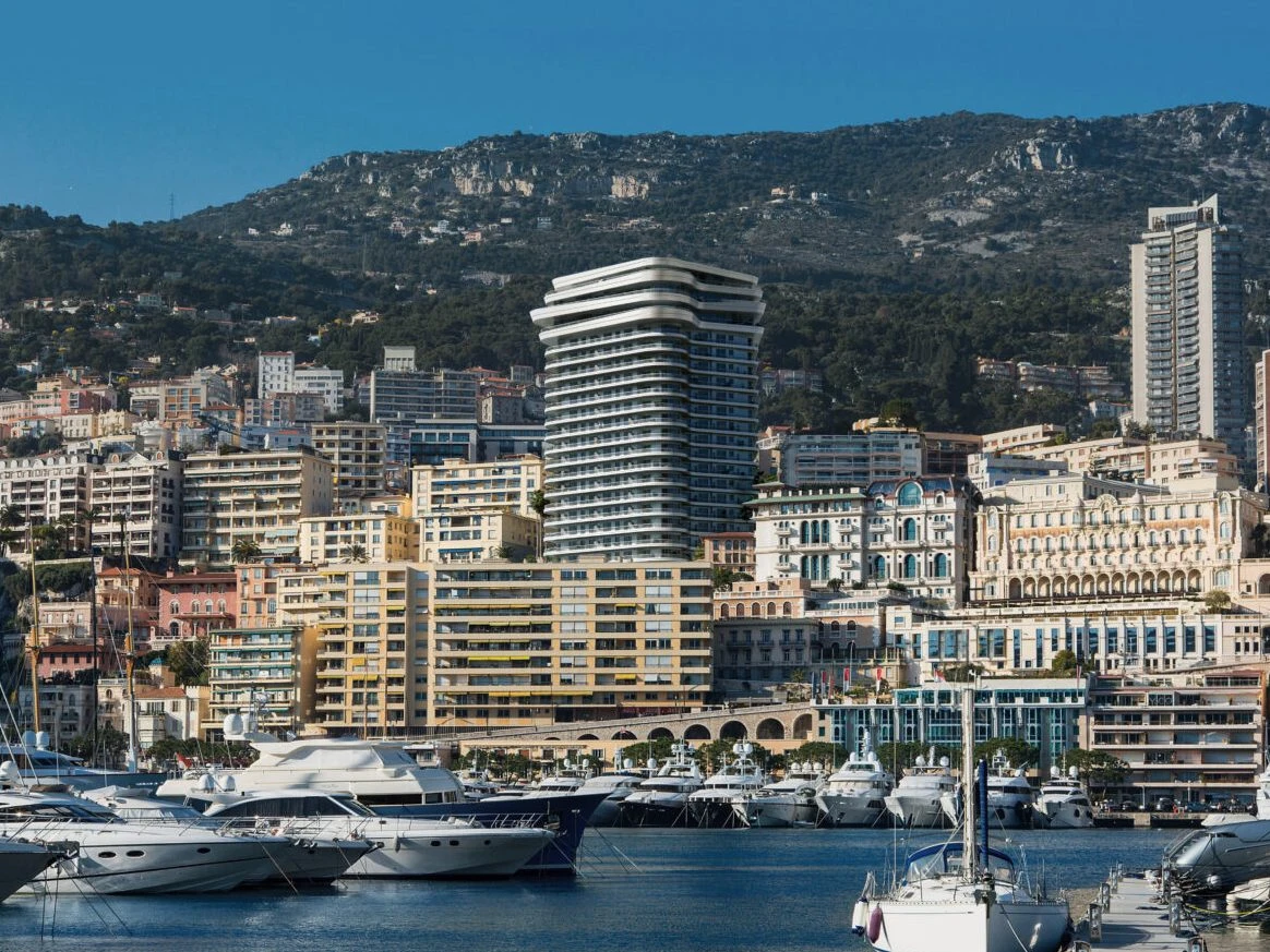 A coastal cityscape with luxury yachts docked in the foreground. In the background, one of Monaco's iconic residences, Le Schuylkill.