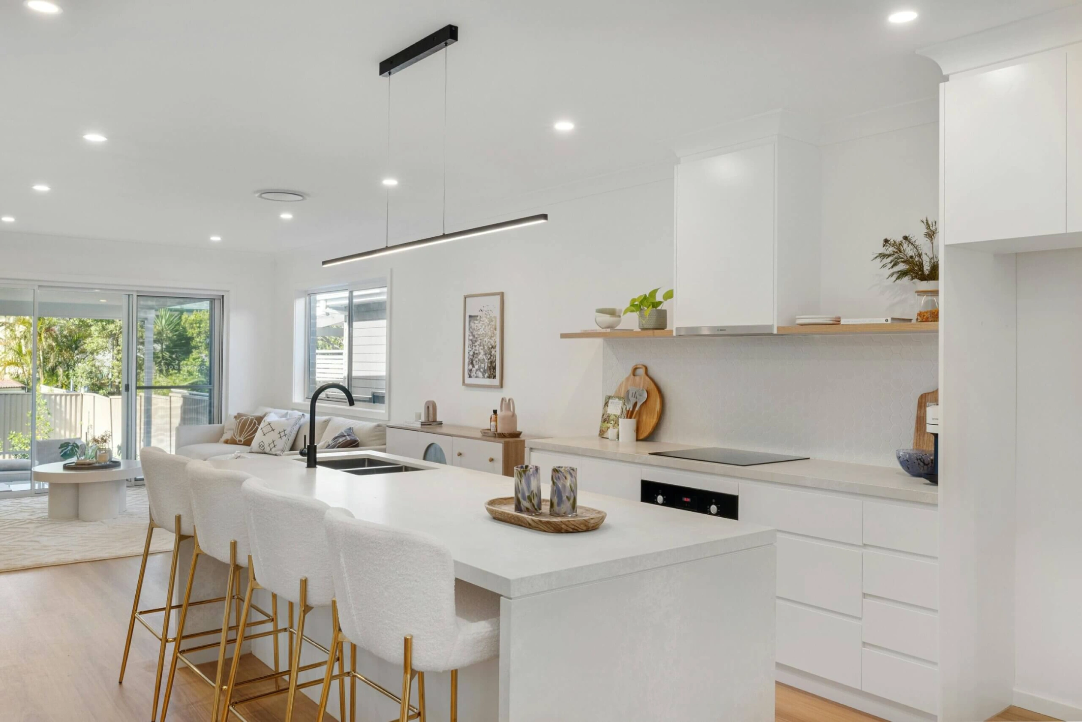 Modern kitchen with white cabinetry, an island featuring white chairs, a sleek black faucet, and a minimalist decor. Bright, airy, and inviting space.