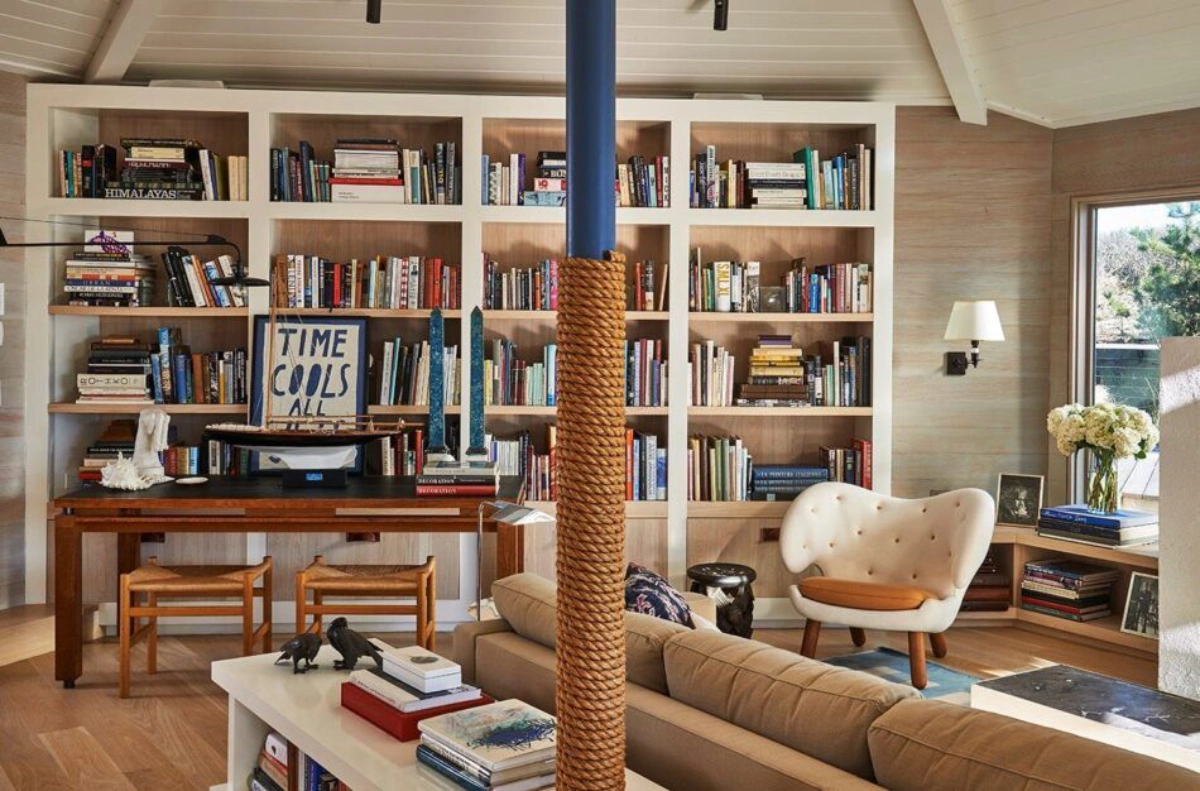 Cozy living room with a large bookcase, filled with books and decor. A unique chair, wooden desk, and cozy sofa create an inviting, warm atmosphere, typical of a reading nook.