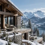 Contemporary luxury Alpine chalet with timber and natural stone architecture, expansive glass walls, layered terraces, and panoramic views of snow-covered mountains, evergreen forests and a deep-blue Alpine lake.